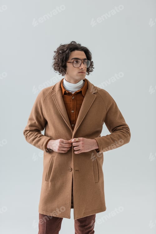 Preview: Stylish young man in eyeglasses buttoning coat isolated on grey