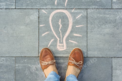 Preview: Female feet with abstract image drawing of light blulb written ongrey sidewalk.