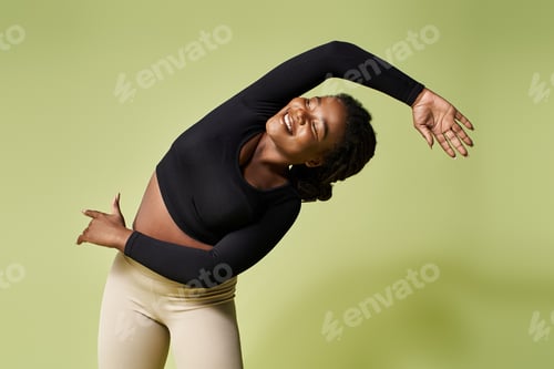 Preview: Fit African American sportswoman demonstrating flexibility in a bright studio