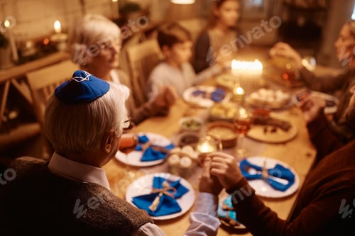 Preview: Rear view of senior man and his extended family praying during Hanukkah meal at dining table.