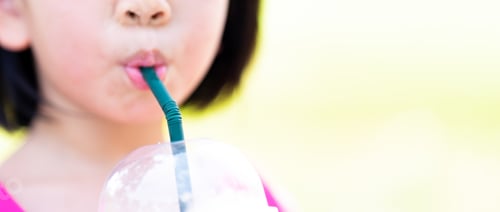 Preview: Cropped imaged. Asian child girl sucking water from a plastic glass with a green straw.