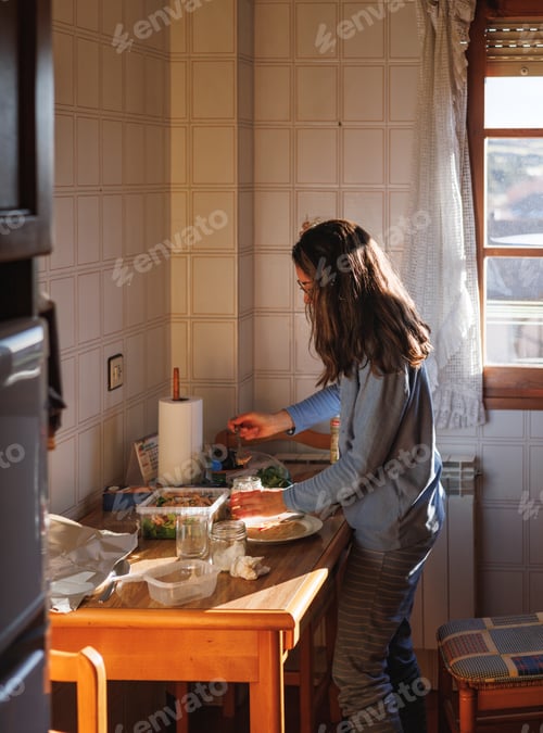 Preview: Young woman in pajamas preparing tupper food at home before going out.