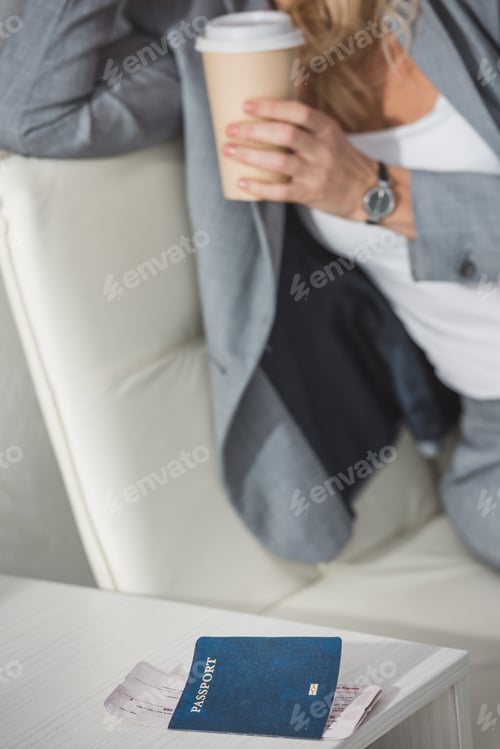 Preview: businesswoman drinking coffee from paper cup with flight ticket on table