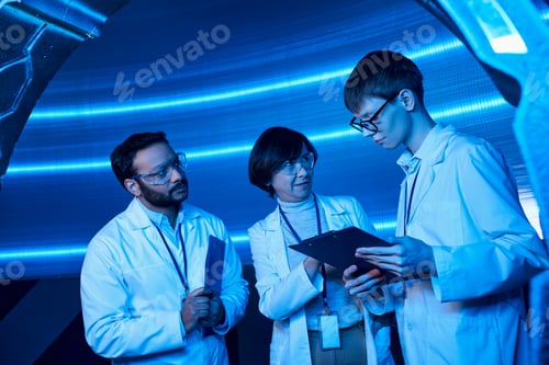 Preview: multiethnic scientists looking at young intern with clipboard in neon-lit futuristic science center