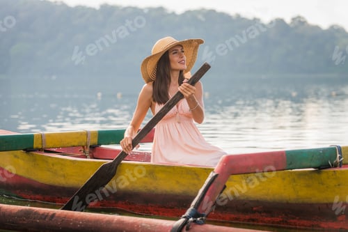 Preview: Young woman traveler paddling on a wooden boat at Pura Ulun Danu Bratan