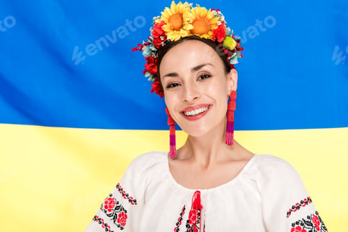 Preview: happy brunette young woman in national Ukrainian costume with flag of Ukraine on background