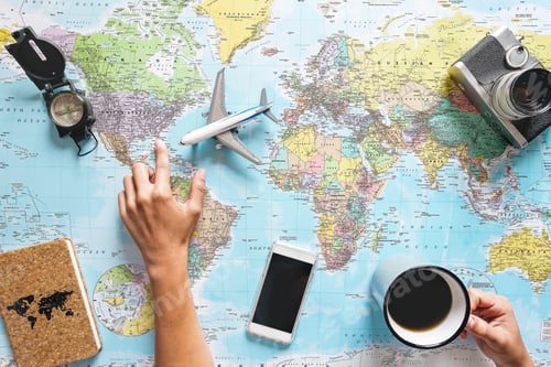 Preview: Top view of young woman planning her vacation using world map while drinking coffee