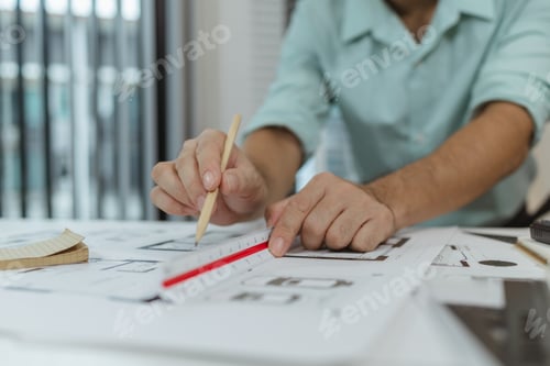 Preview: An architect using a pencil and a scale ruler to measure house floor plans.