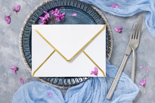 Preview: Wedding table place with envelope near fabric and wild purple flowers top view on gray, mockup