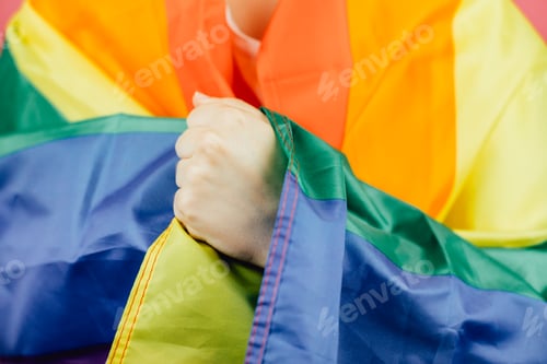 Preview: Close up hand over flag. Woman smiling happily to camera while holding a LGBTIQ