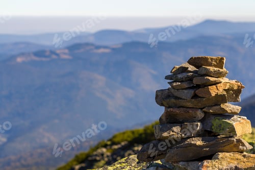 Preview: Stack of stones covered with moss on top of a mountain on mountains background.