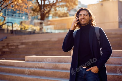Preview: Happy businessman talking on mobile phone while walking on the street.