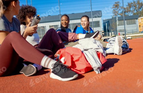 Preview: Diverse group of young woman sitting on court resting afrer playing basketball outdoors.