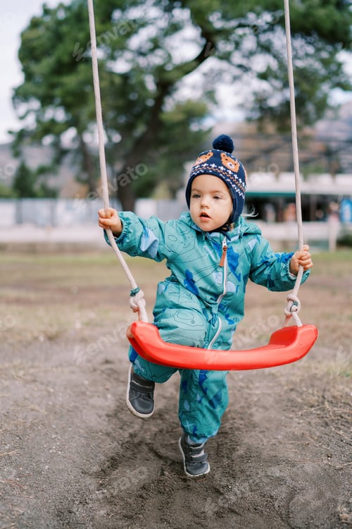 Preview: Little girl is standing, leaning her knee on a rope swing