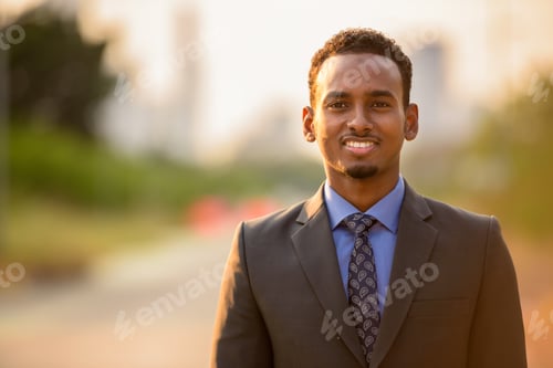 Preview: Handsome young black businessman wearing suit in city while smiling
