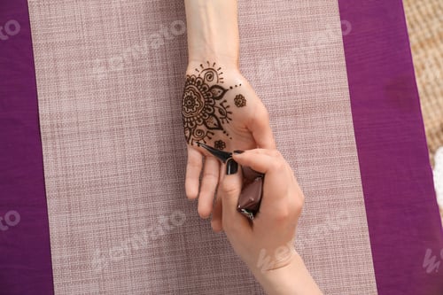 Preview: Professional mehndi master making henna tattoo at table, top view