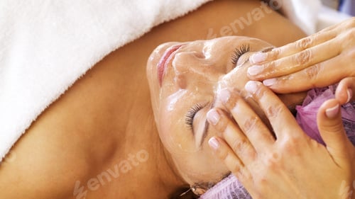 Preview: Woman in a spa salon on cosmetic procedures for facial care. Cosmetologist applies a cosmetic cream.