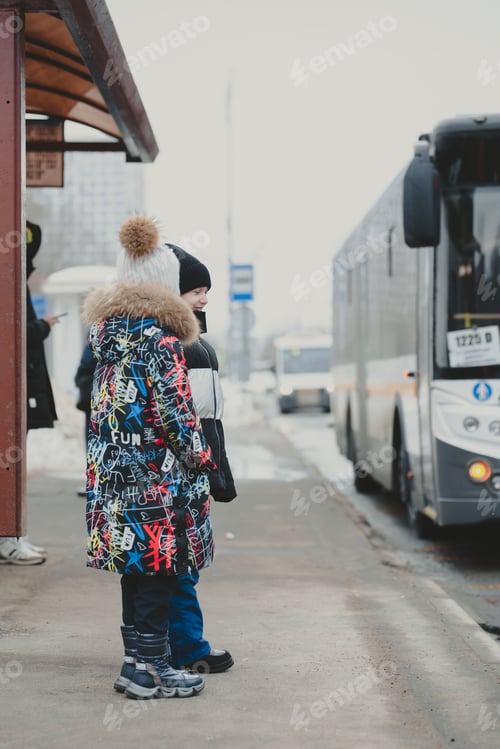Preview: The girls are standing at a bus stop in winter and a white bus pulls up.