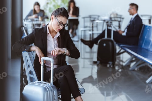 Preview: adult businesswoman looking at watch and waiting for departure in airport