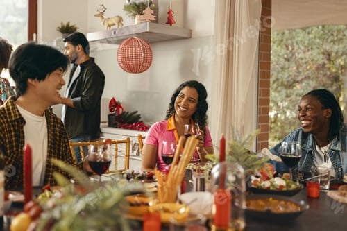 Preview: Happy friends enjoying in conversation and drinking wine during festive dinner at home party