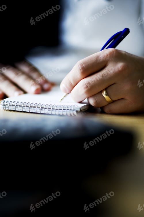 Preview: Cropped image of man writing in note pad at table