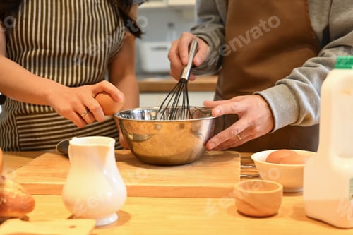 Preview: Cropped shot of young couple in apron preparing dough for homemade pancakes.