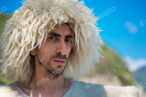 Preview: A Georgian man in a hat against the background of mountains and the sky. Selective focus.