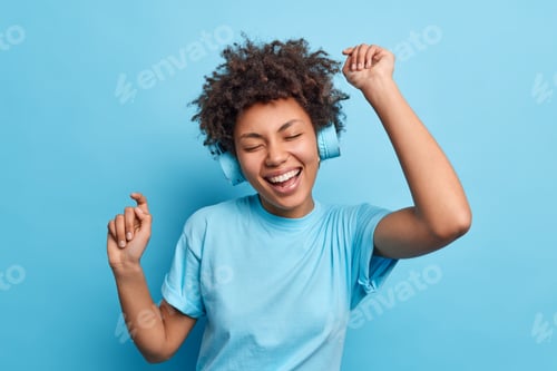 Preview: Joyful relaxed African American girl enjoys favorite playlist listens music via wreless headphones r