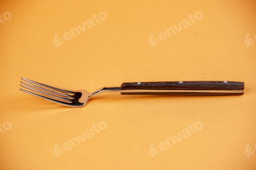 Preview: Front close view of shiny stainless metal fork lying on peach color background with free space