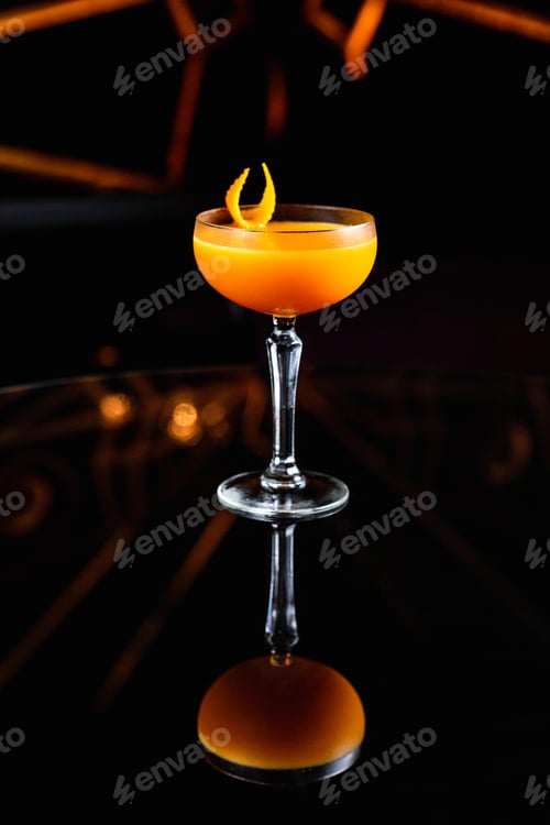 Vista previa: Cóctel de naranja y cítricos en una copa cupé, adornado con piel de naranja sobre una mesa negra con reflejos