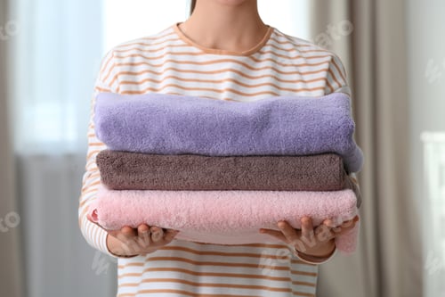Preview: Young woman holding clean laundry at home, closeup