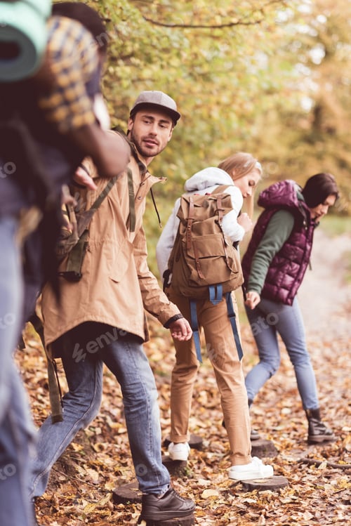 Preview: Four young friends backpackers walking in row in autumn forest