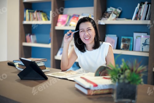 Preview: Portrait beautiful Asian woman works at the home office with blurred shelf of books in background