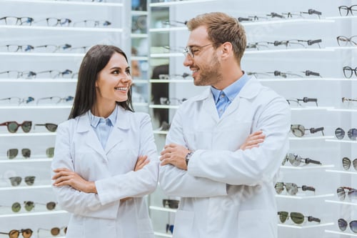 Preview: professional smiling doctors posing with crossed arms in ophthalmic shop with eyeglasses