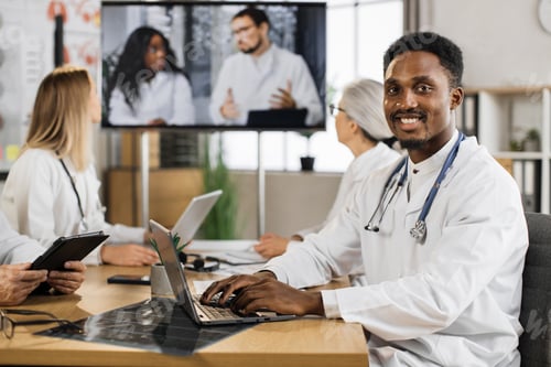 Preview: African american male physician with stethoscope working on laptop during online conference