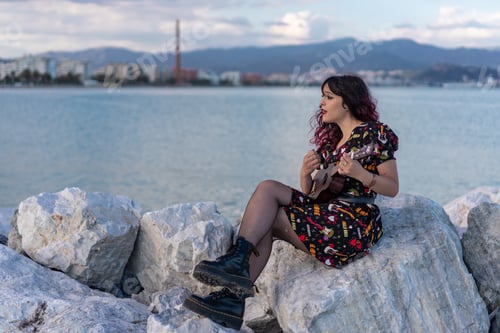 Preview: Caucasian female with red hair playing ukulele near the sea