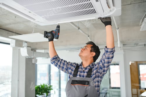 Preview: Concentrated young Indian engineer setting up air conditioner.