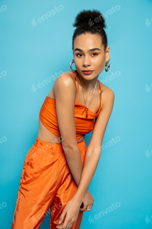 Preview: stylish african american model in striking orange outfit with golden accessories looking at camera