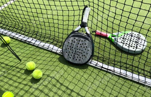 Preview: Padel racket and padel ball on a green court in the sunset