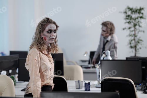 Preview: Young zombie businesswoman walking between desks with computer monitors against dead male colleague