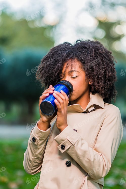 Preview: Drinking coffee drink outdoors in winter from a thermos. Latinx woman with afro curly hair