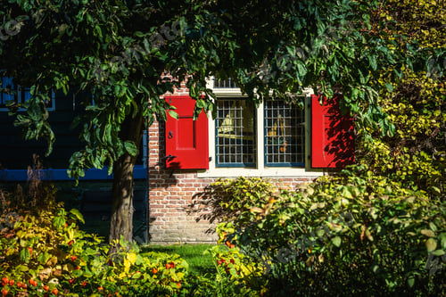 Preview: Exterior of an old brick building with a bright red and white windows covered with greenery