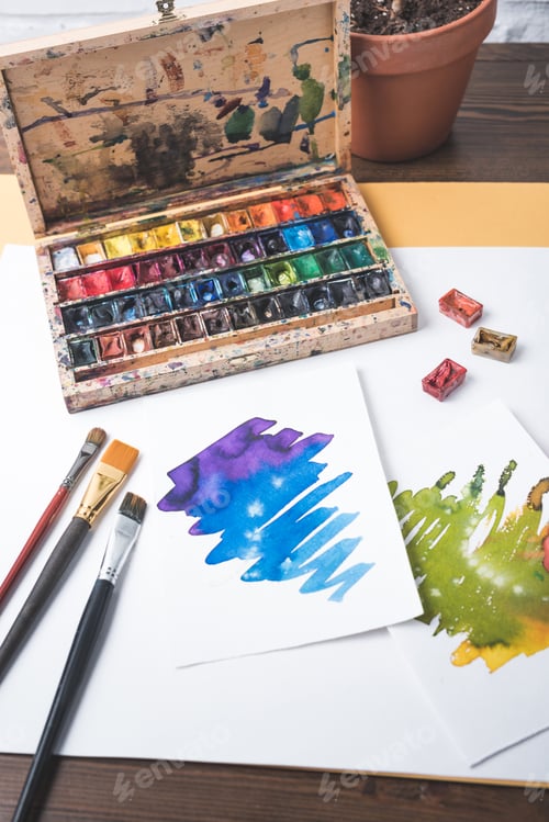 Preview: top view of paints, paintbrushes and watercolor sketches at designer workplace