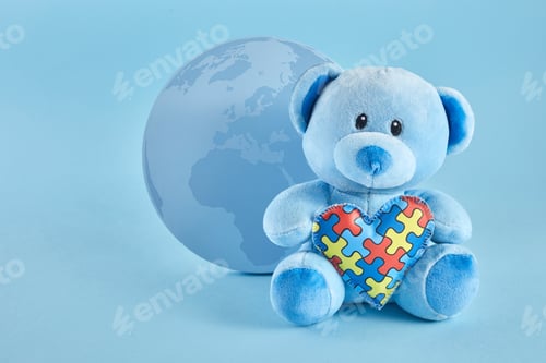 Preview: World Autism Awareness, concept with teddy bear holding puzzle or jigsaw pattern heart on blue