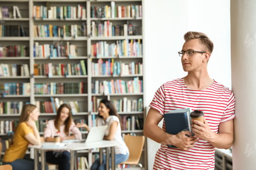 Preview: Young man with books and drink in library. Space for text