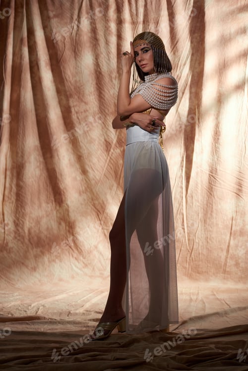 Preview: Full length of stylish woman in egyptian look and bold makeup standing on abstract background