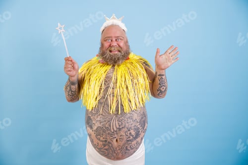 Preview: Joyful bearded plump man with crown, magic stick and yellow cape on light blue background