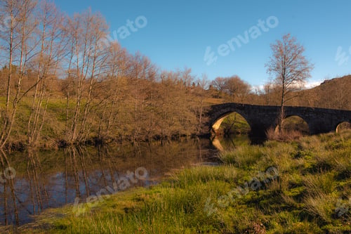 Preview: Old bridge over calm river in autumn countryside