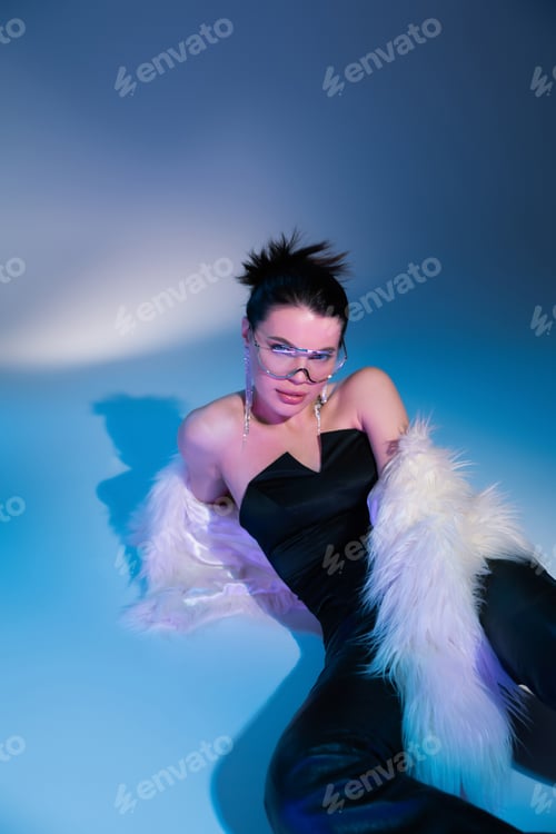 Preview: sensual brunette woman in black corset and white fluffy jacket lying on blue background