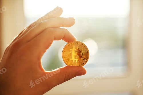 Preview: Hand holding shiny golden bitcoin in light, gold money